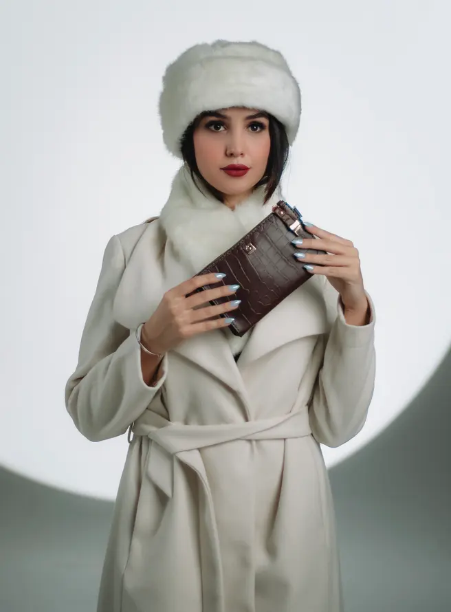 A model in a white winter outfit holding a brown clutch bag.